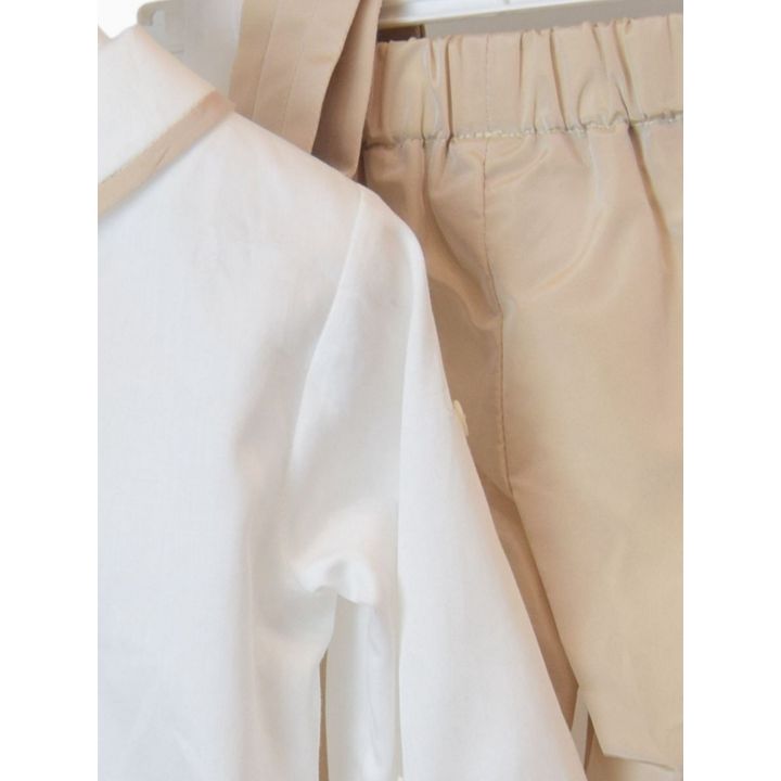 Dettaglio della manica della camicia e del pantalone beige con elastico in vita