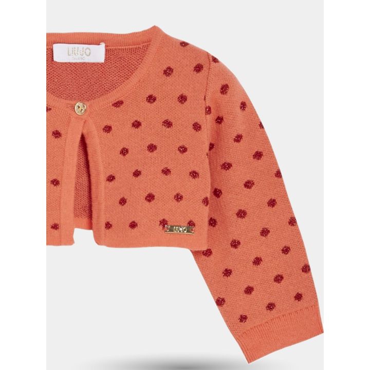 Dettaglio del cardigan corallo a pois con bottone dorato e manica lunga