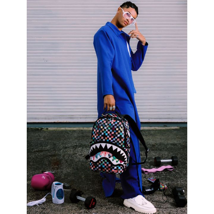 Ragazzo vestito di blu con lo zaino Sprayground Crazy Check in mano