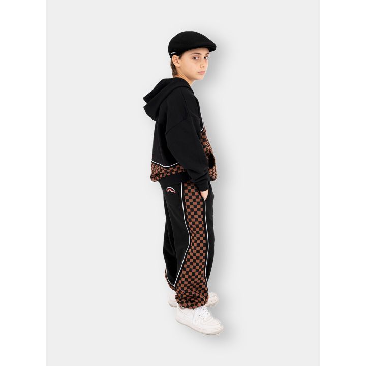 Ragazzo di profilo con pantaloni e felpa Sprayground a scacchi marroni