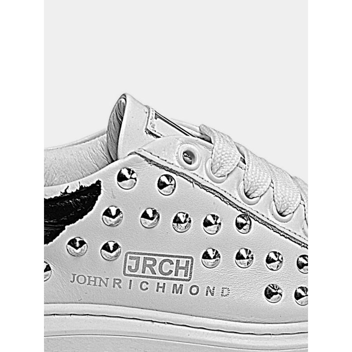 Dettaglio delle borchie e del logo JRCH sul fianco delle sneakers bianche